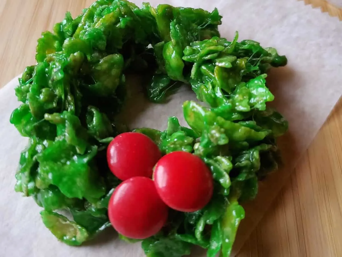 Image shows Holly Wreath Cookies on small pieces of parchment paper sitting on a wooden table.