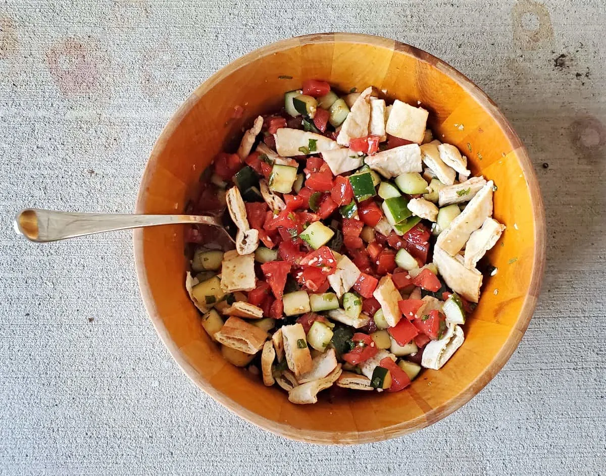 Overhead shot of a wooden bowl of Greek panzanella salad sitting on concrete.