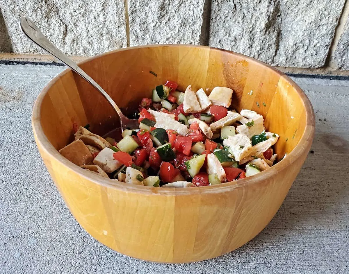 Photo of a wooden salad bowl with cucumber tomato salad inside.