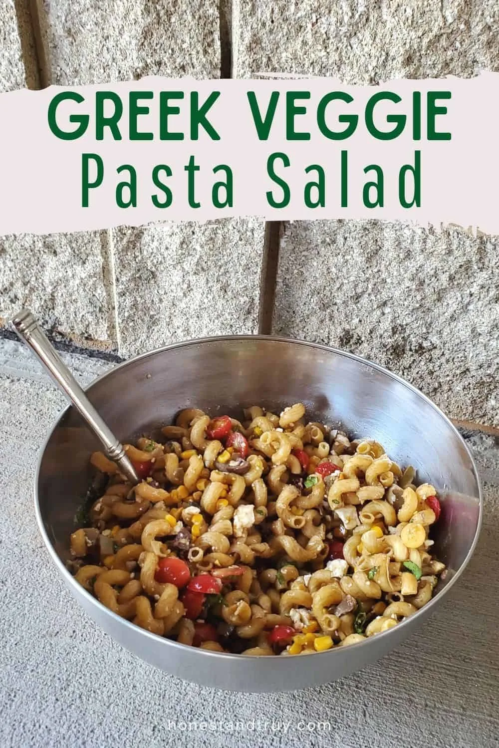 Greek veggie pasta salad in a bowl with a stone wall behind.