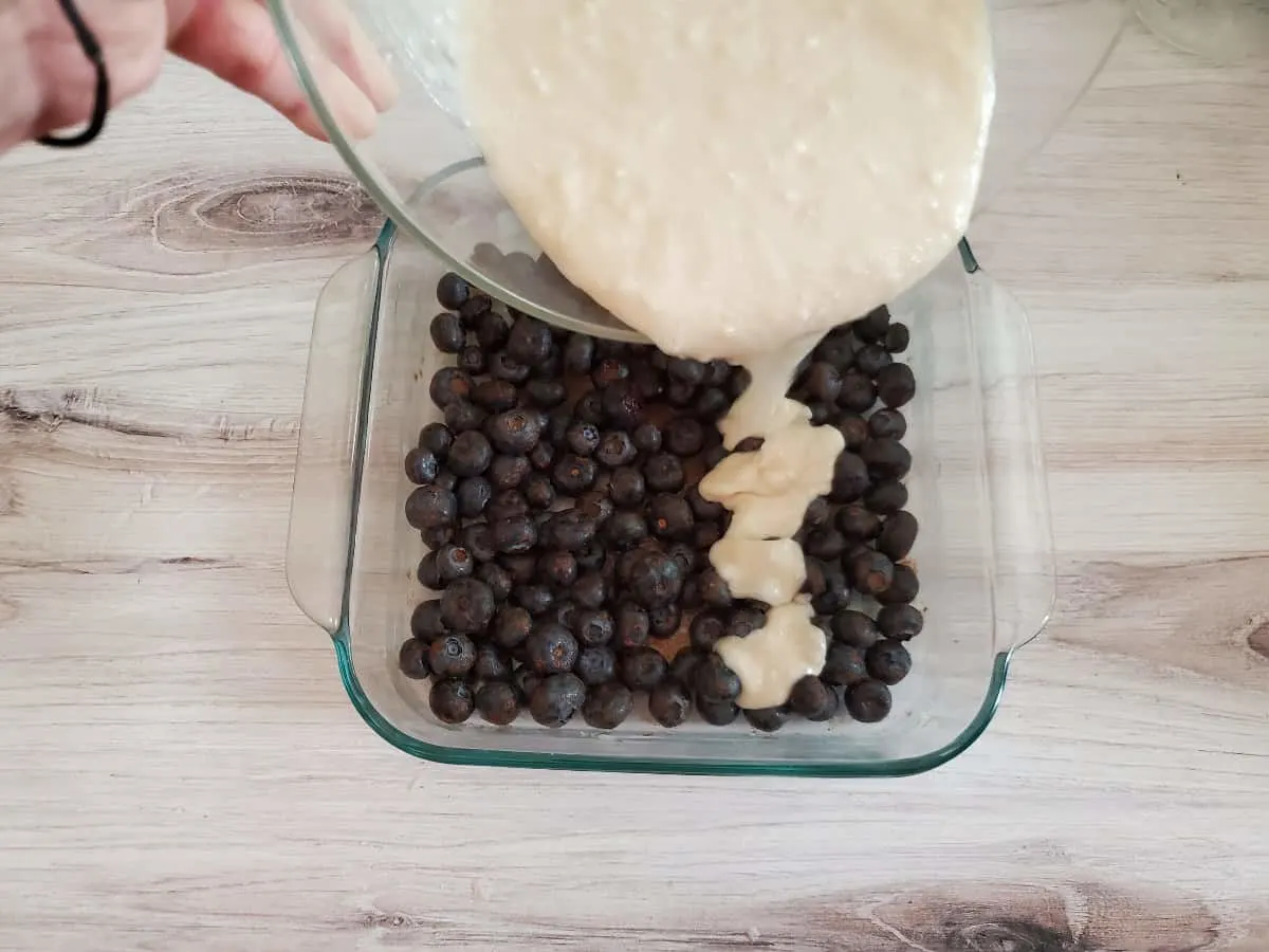 Pouring cake batter over blueberries.