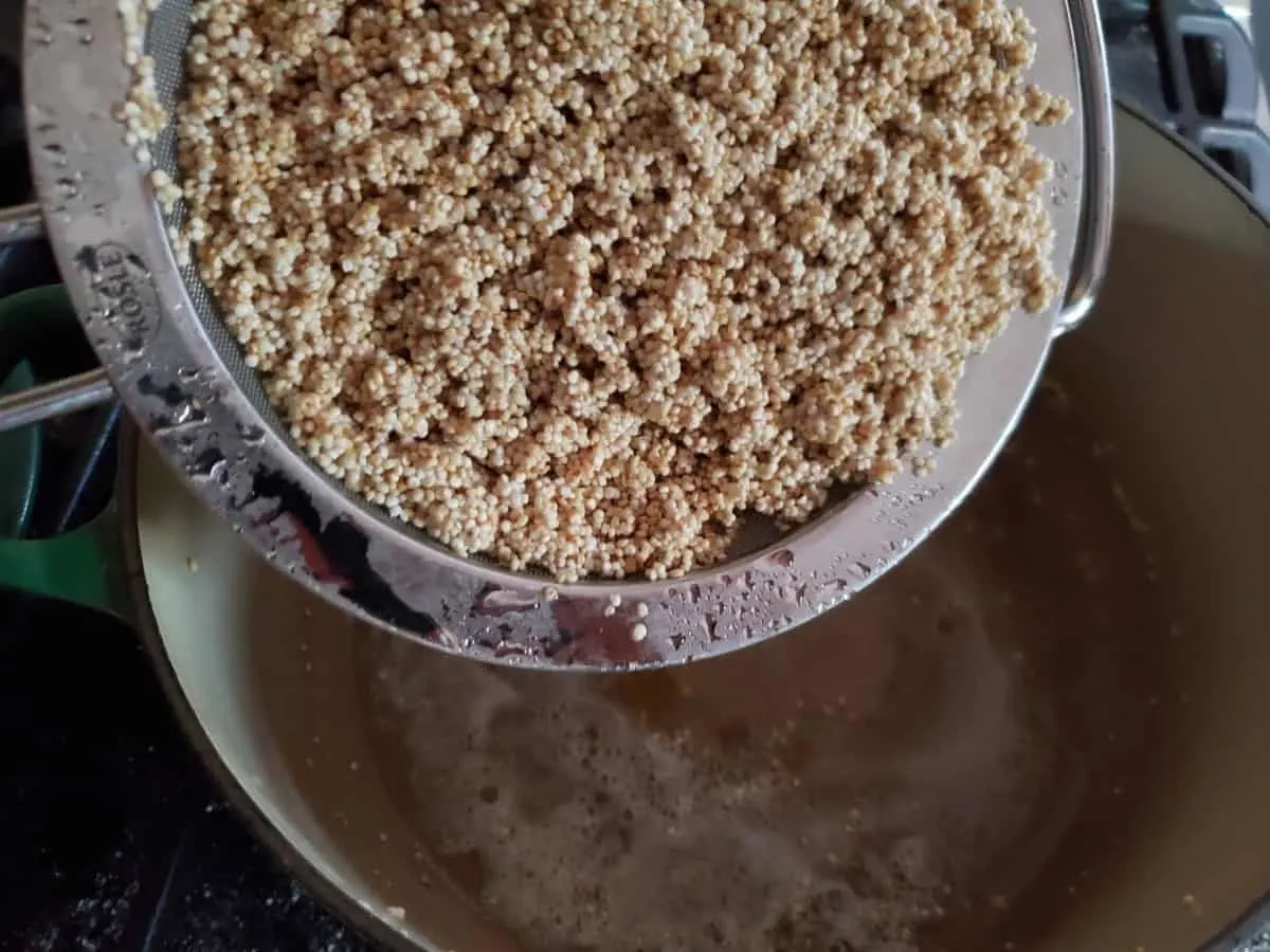 Adding cleaned quinoa to a cast iron pot with melted butter in it.