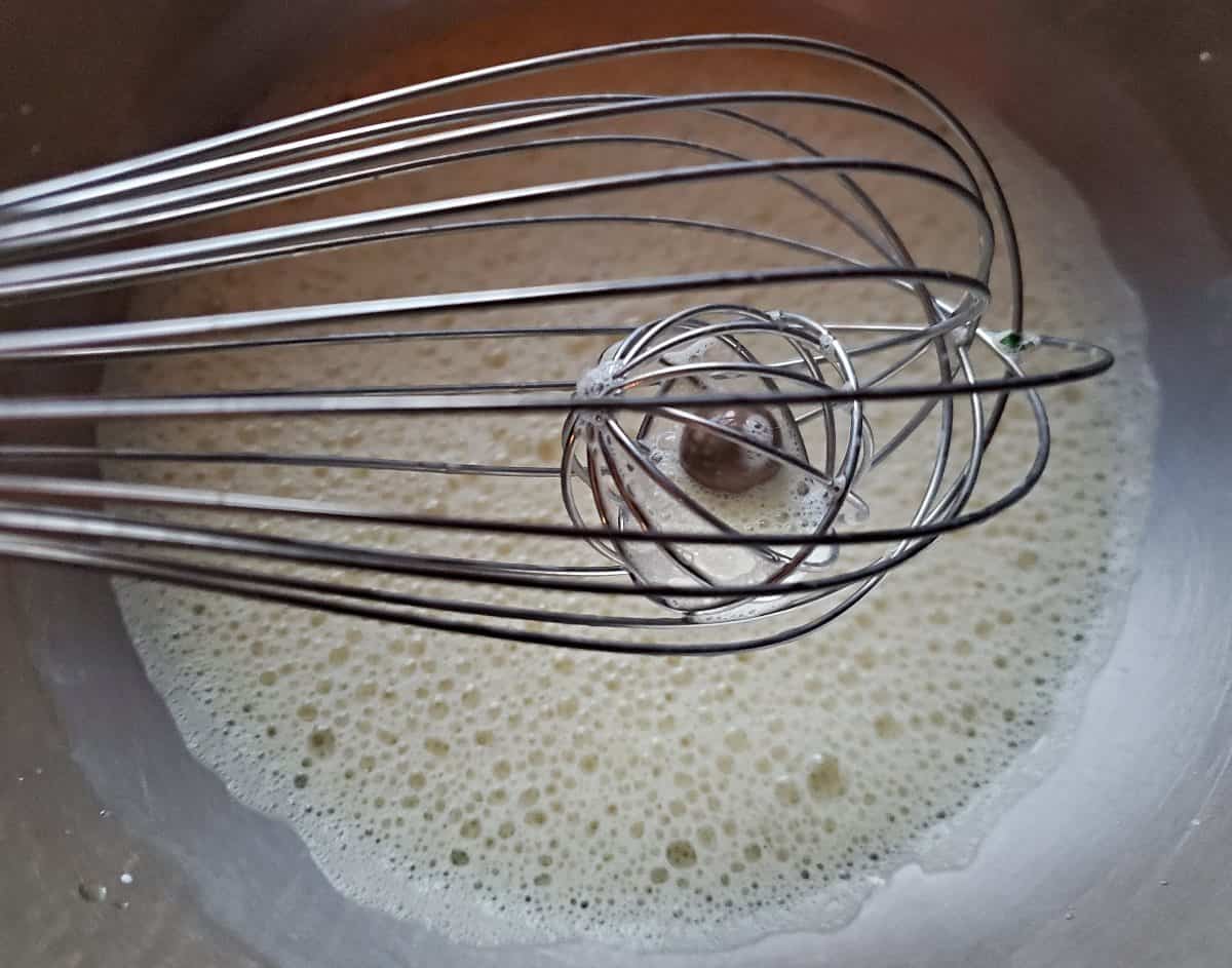 Basket whisk held above a silver bowl with whipped eggs.