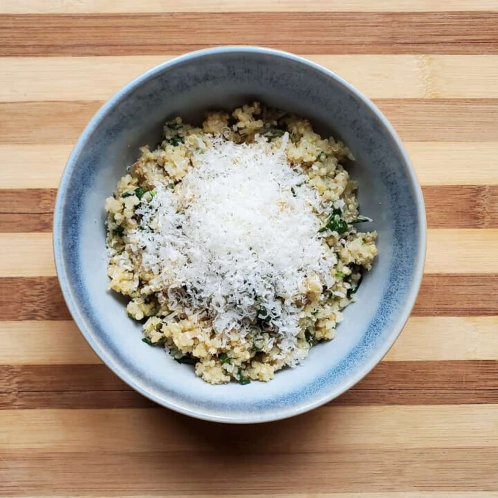 Bowl of spinach quinoa topped with parmesan cheese on a striped wooden board