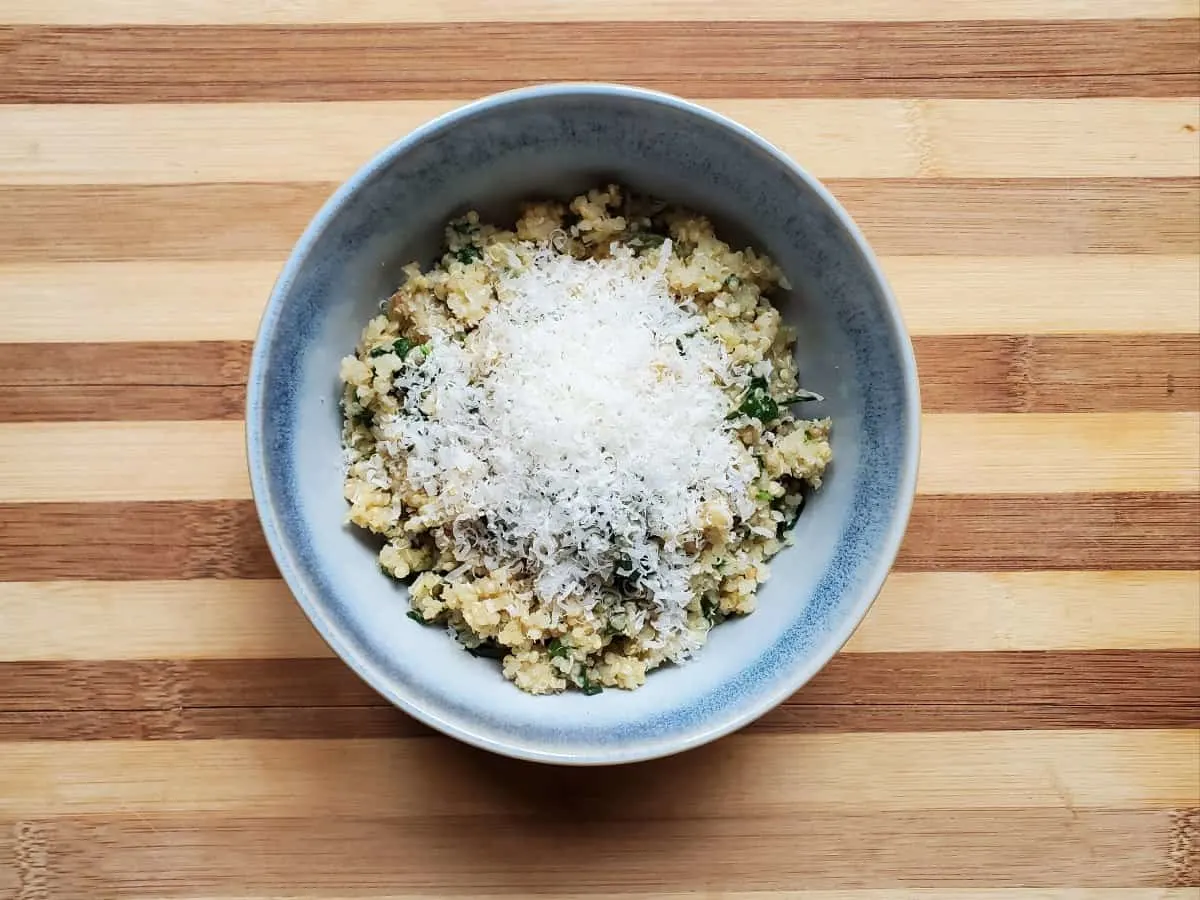 Image shows an overhead shot of Spinach Parmesan Quinoa in a blue bowl with a sprinkle of cheese on top.