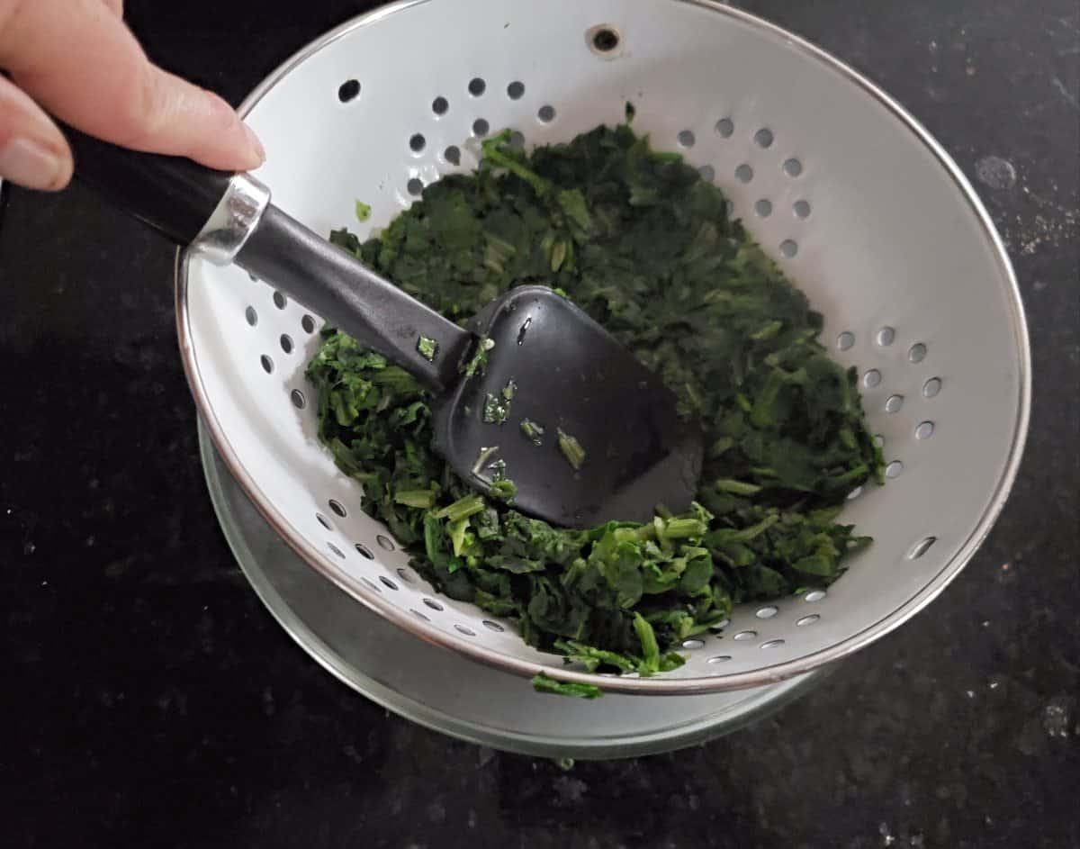 Draining spinach in a colander with a spatula to press out liquid.