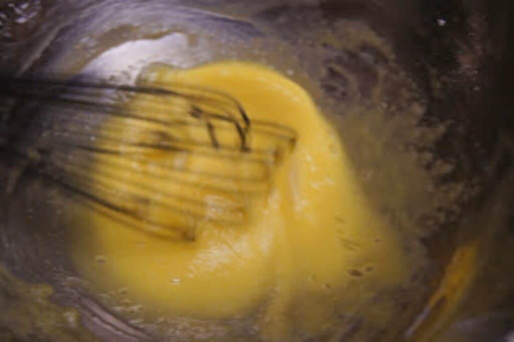 Egg yolks being whisked in a silver bowl.