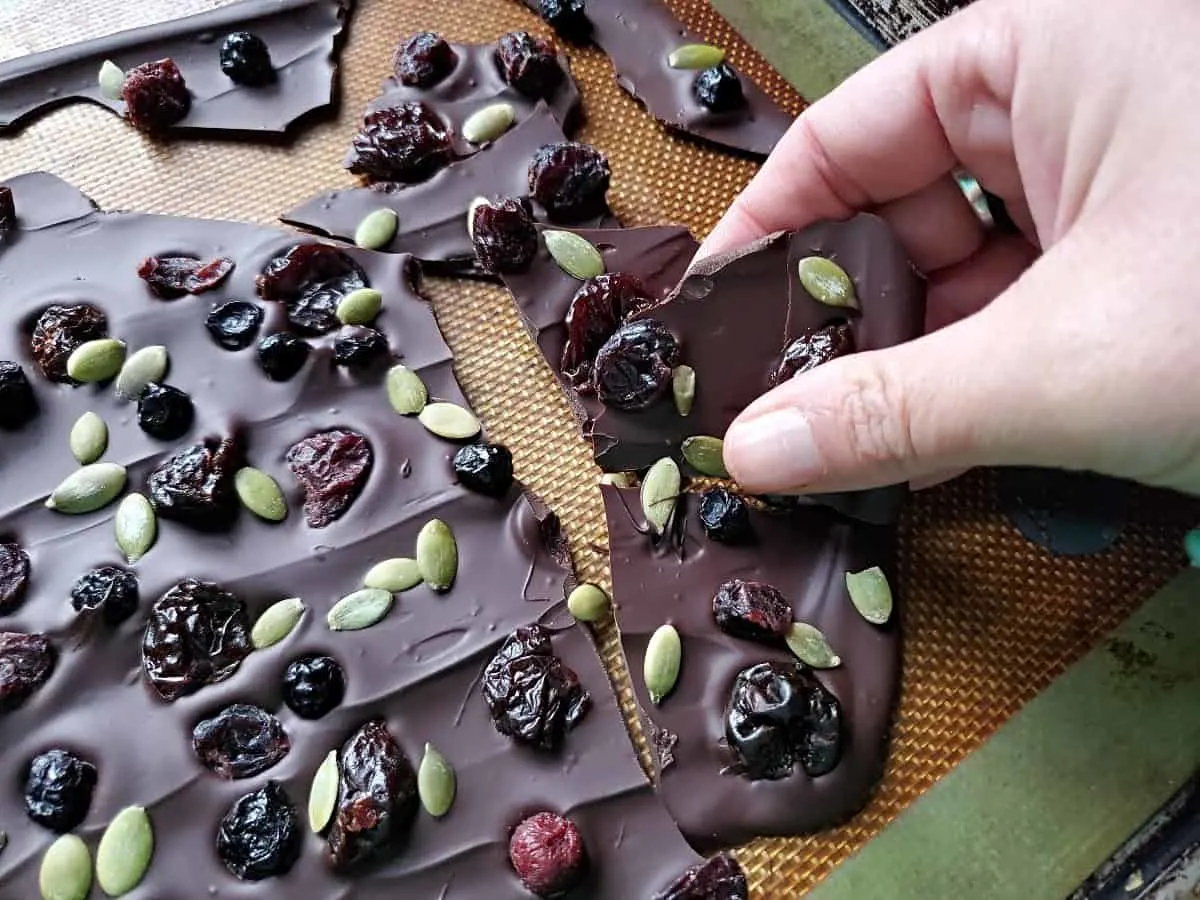 A hand breaking antioxidant chocolate bark into pieces on a silpat.