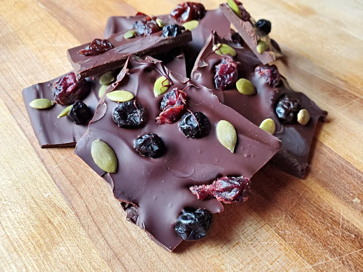 Closeup of dark chocolate bark with dried fruit on a wooden background.