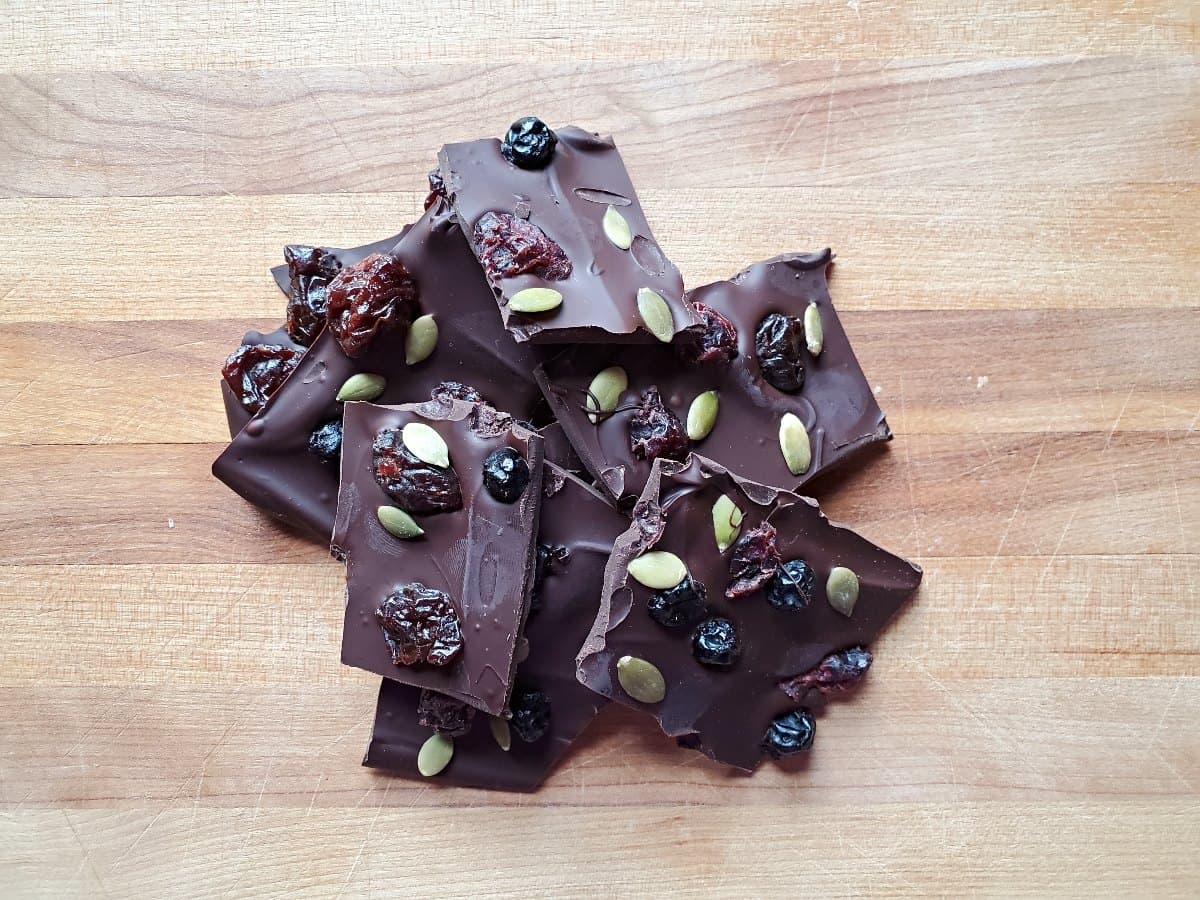 Pile of dark chocolate bark with dried fruit on a wooden background.