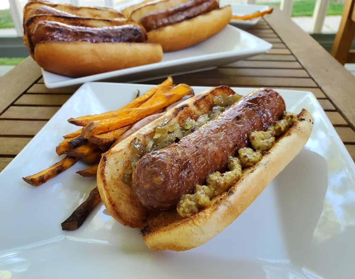 Bratwurst with mustard and relish on a plate with more in the background.