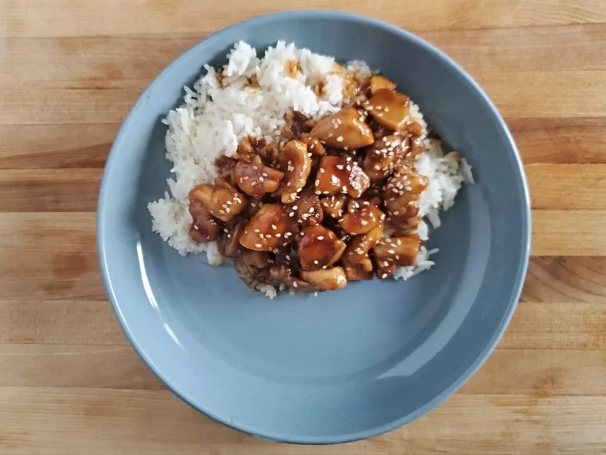 Honey glazed chicken over rice on a blue plate.