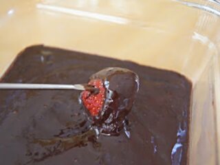 Dipping a strawberry on a fondue fork into chocolate fondue.