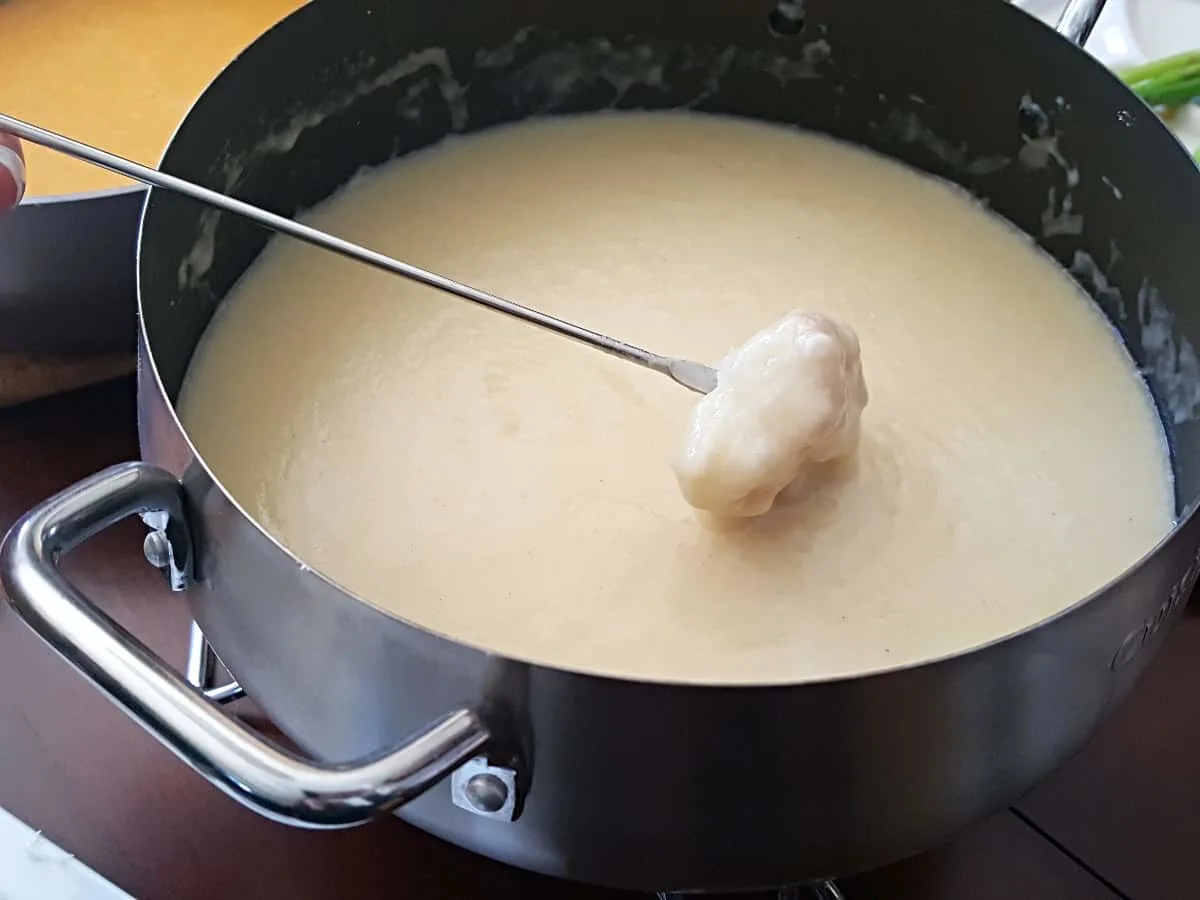 Dipping bread into traditional cheese fondue with a fondue fork.