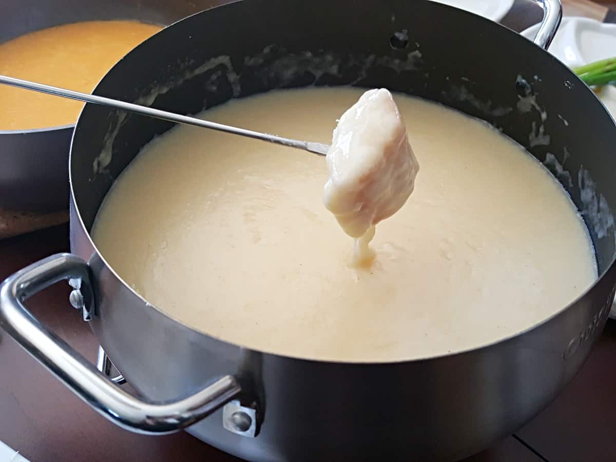 Fork with a chunk of bread dripping cheese fondue.