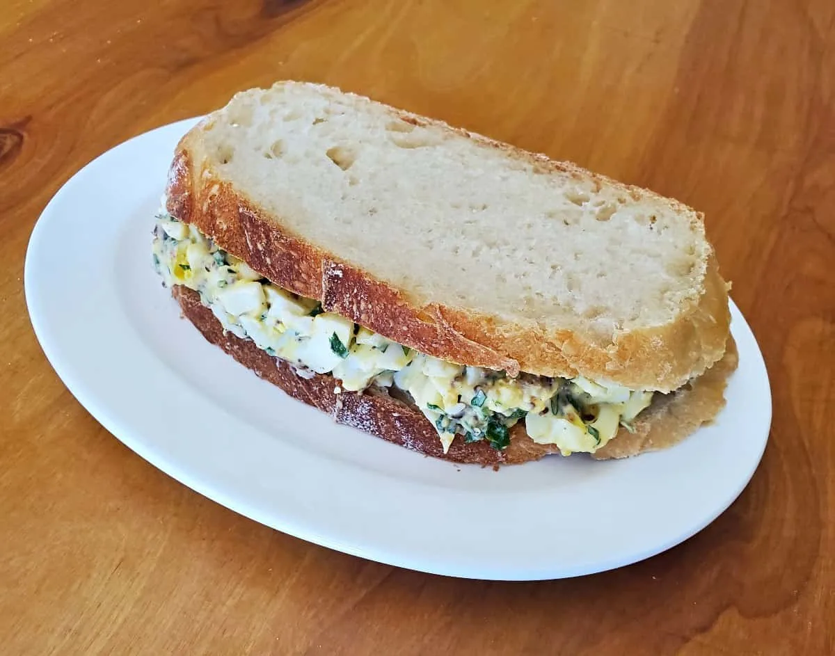 Bacon egg salad sandwich on a white plate.