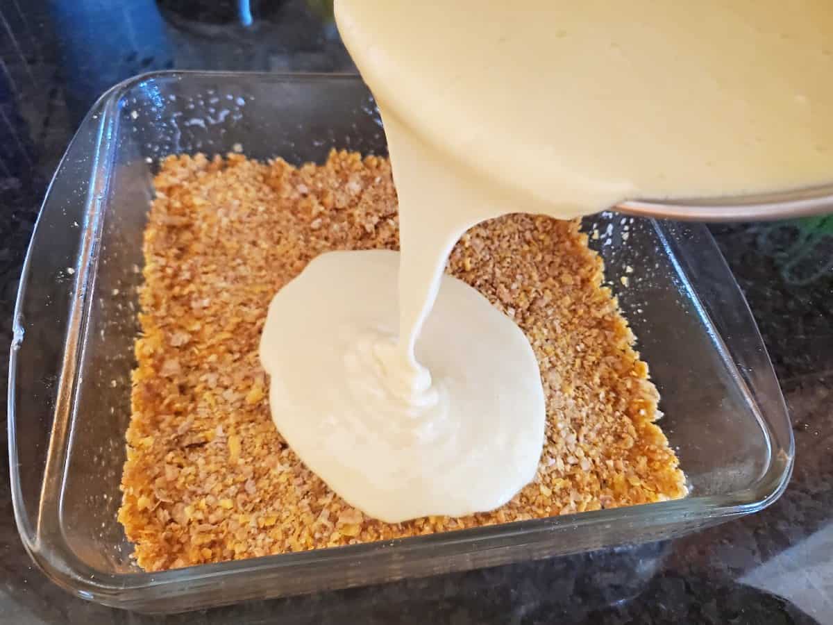 Pouring orange cheesecake batter over cereal crust.