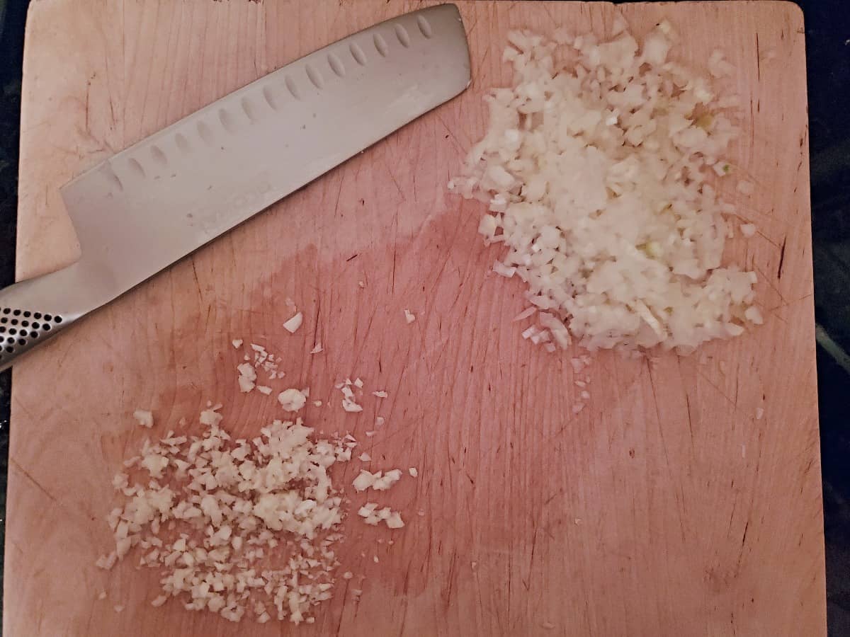 Minced onion and garlic on a wooden board.