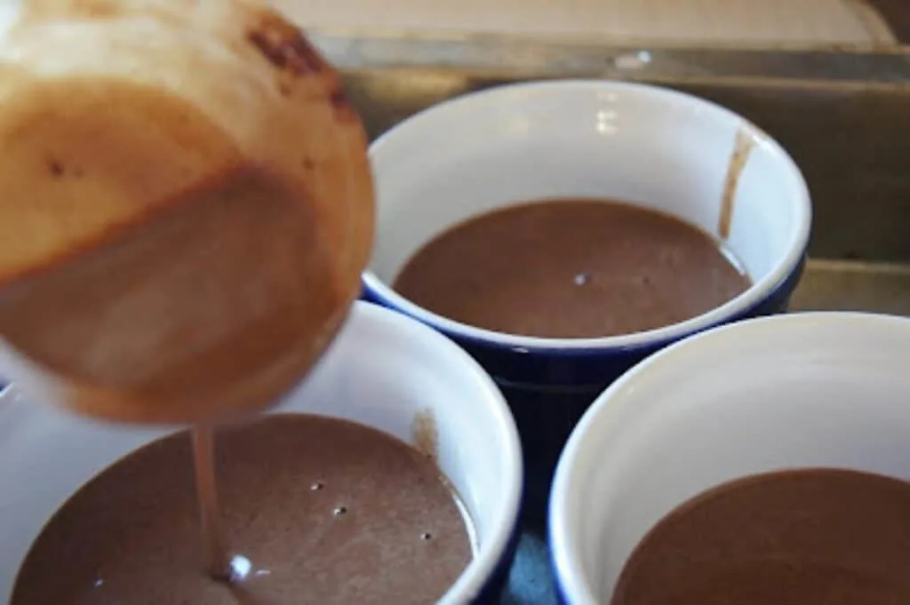 Pouring pots de creme into ramekins with a measuring cup.