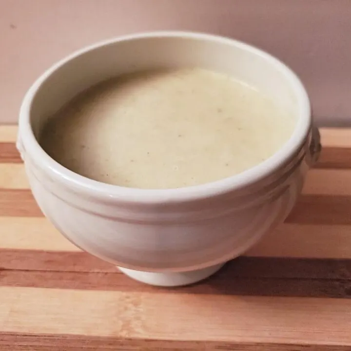 White bowl of homemade cream of celery soup on a wooden table.