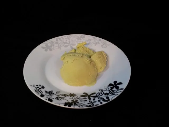 Two scoops of avocado ice cream on a plate with a black background.
