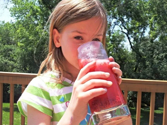 Girl drinking a glass of berry lemonade.