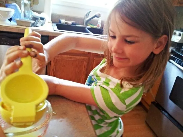 Girl squeezing lemons into a measuring cup.