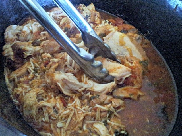 Shredding chicken in the pot with tongs