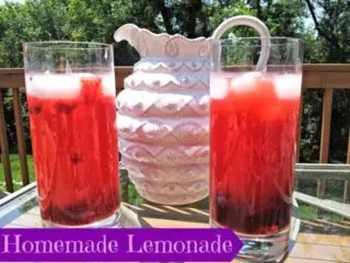 Two glasses of homemade berry lemonade in front of a white pitcher with text homemade lemonade.