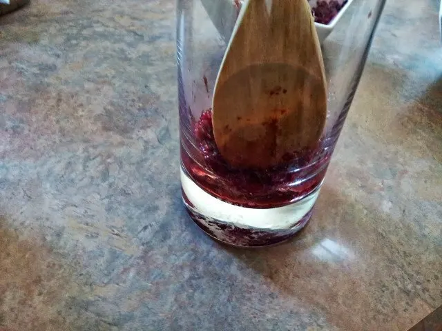 Wooden spoon muddling berries in a tall glass.