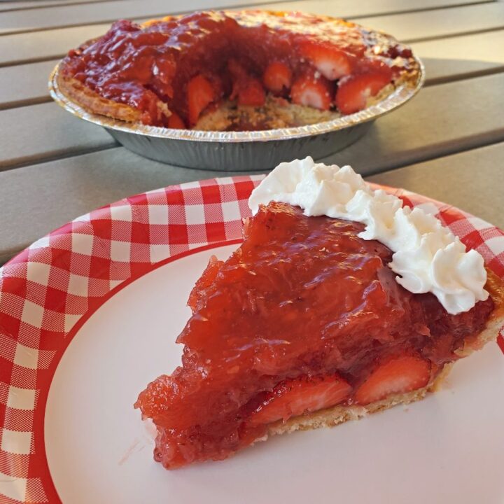 Close up of fresh strawberry pie slice with the remaining pie in the background.