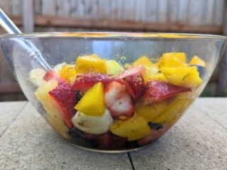 Image shows a Bowl with tropical fruit salad on a stone table.