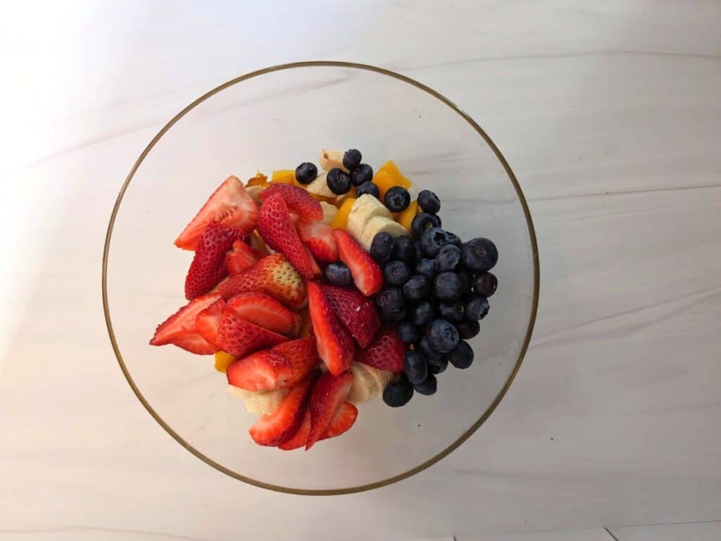 Image shows an overhead shot of Chopped fruit in a bowl.