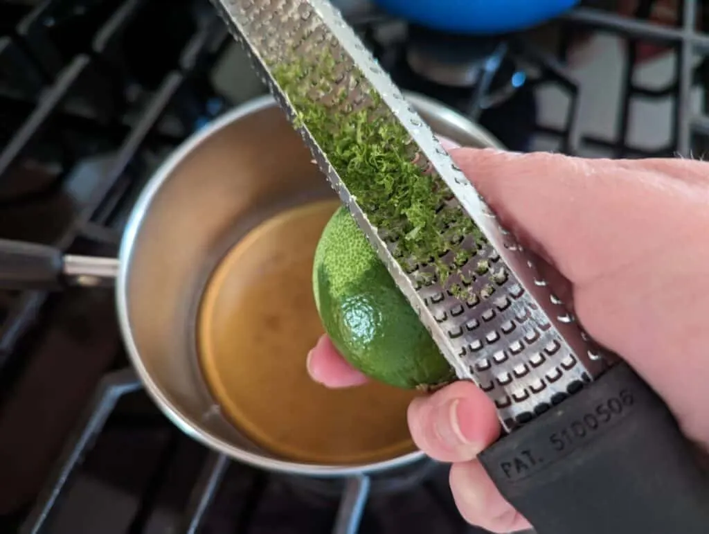 Image shows a hand Zesting a lime over a pot.