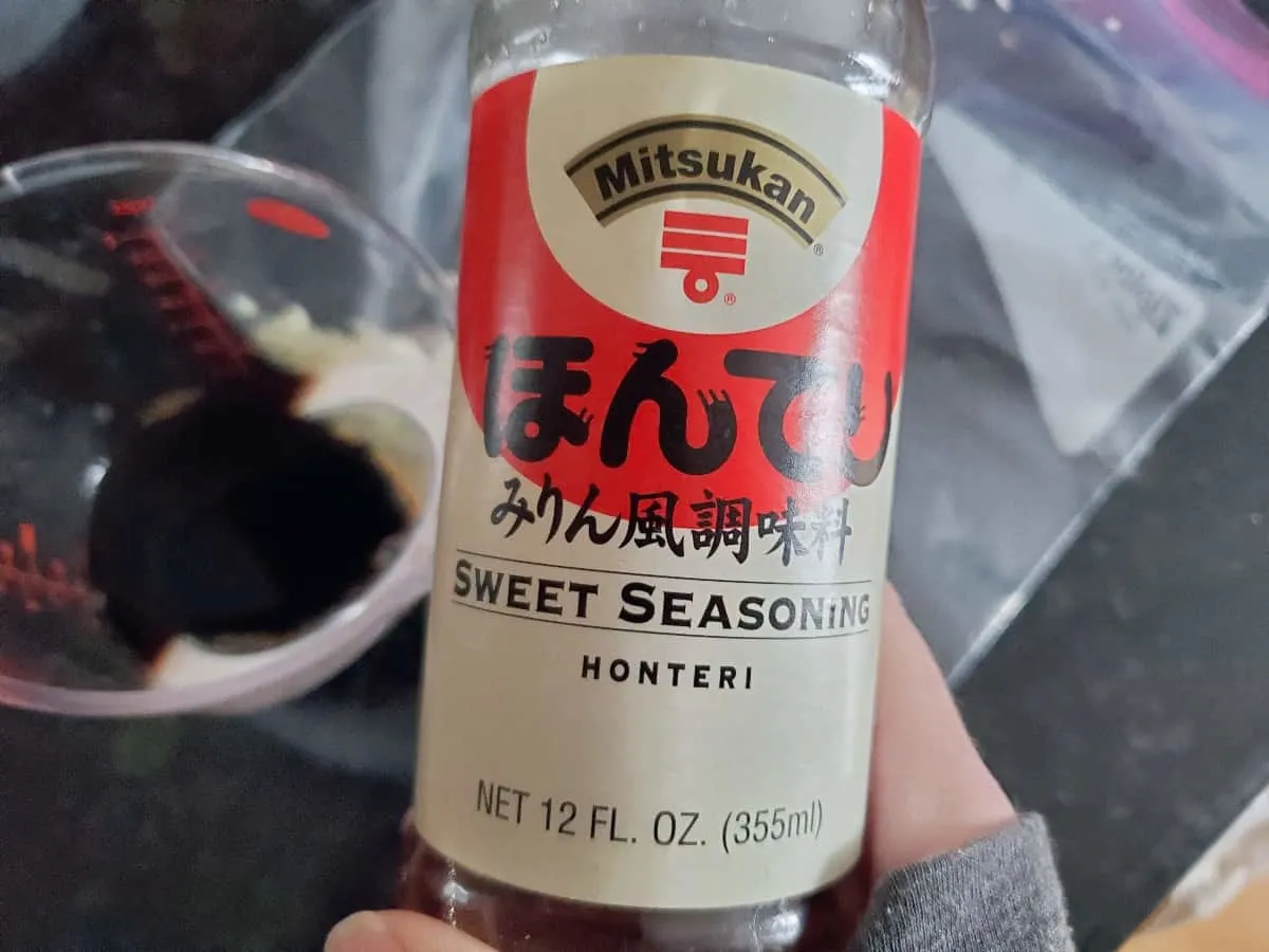 Hand holding a bottle of Asian sweet seasoning sauce.