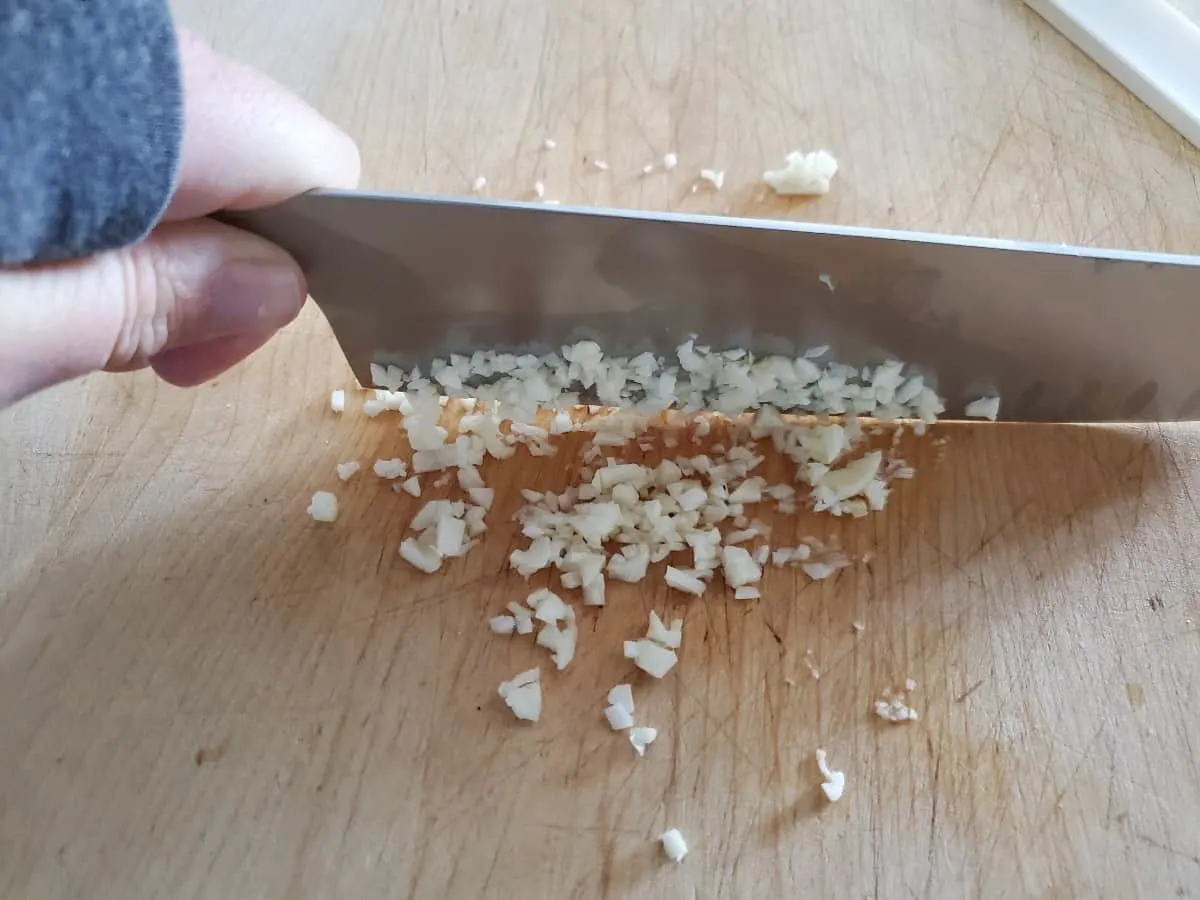 Knife mincing garlic on a wooden board.