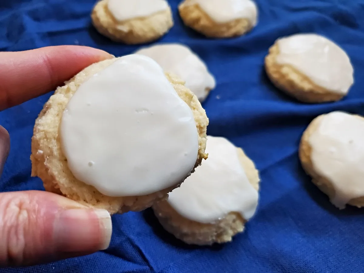 Image shows a fingers holding a Chewy Lemon Cookie with more in the background.