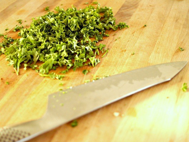 Freshly chopped parsley on a cutting board with a knife in front of it.