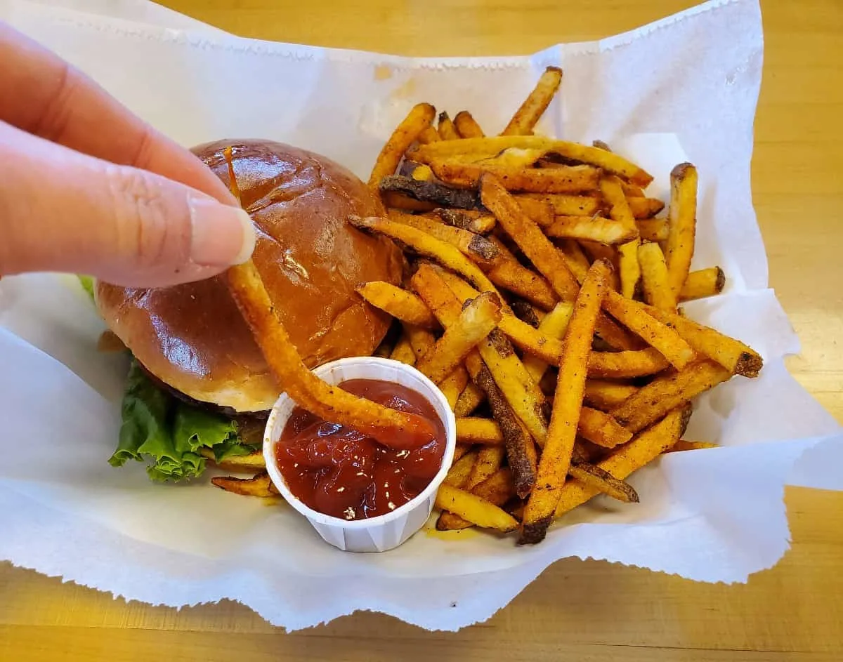 Dipping a french fry in ketchup that's sitting in a burger basket.