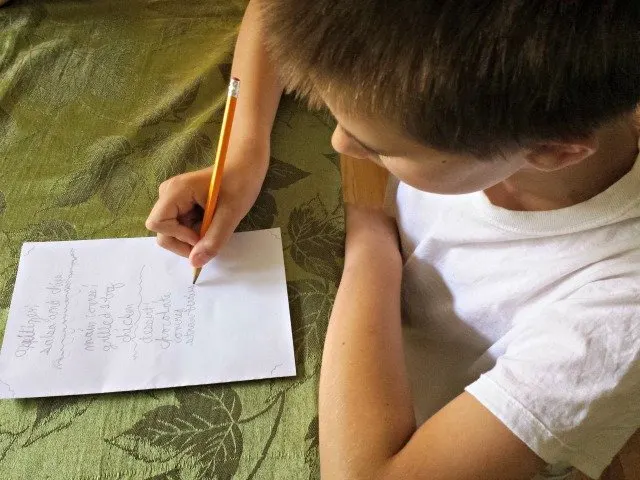 Boy writing a menu on a piece of paper.