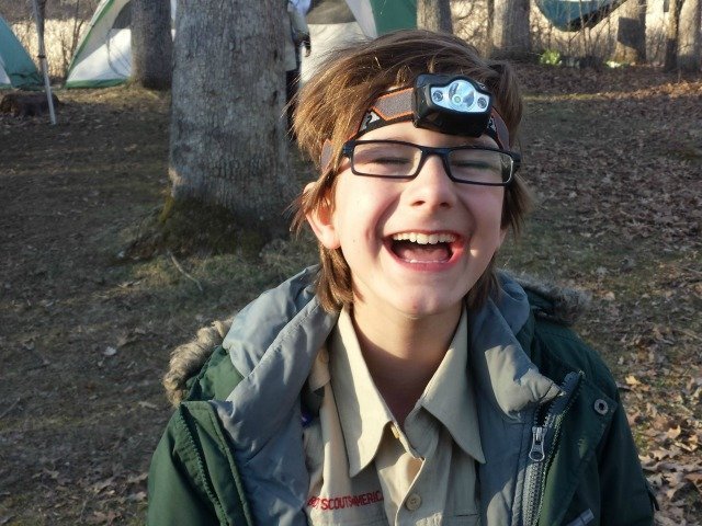 Boy laughing in the woods wearing a helmet light.