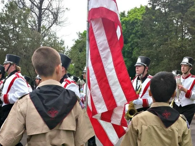 Boy Scouts saluting a veteran band in a parade.