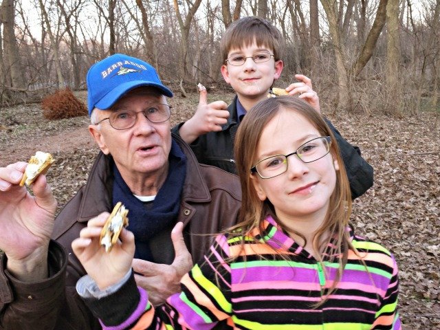 Grandfather with two grandchildren eating s'mores.