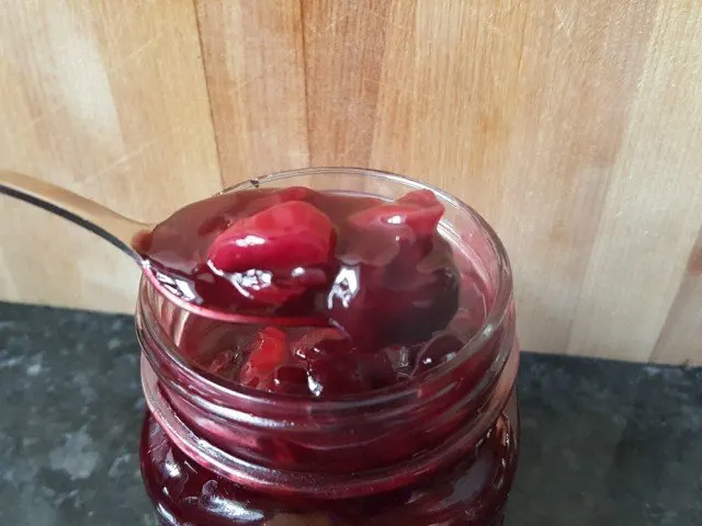 Cherry syrup in a jar with a spoon scooping some out.