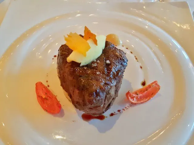 Broiled Filet Mignon sitting on a round white plate with decorative accompaniments.