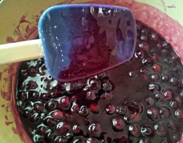 Thickened blueberry compote sticking to a spatula over the pot.