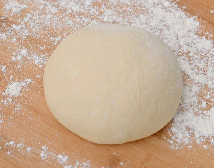 Homemade pizza dough ready to roll out on a wooden board.