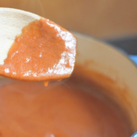 Homemade enchilada sauce dripping off a spoon into the pot.