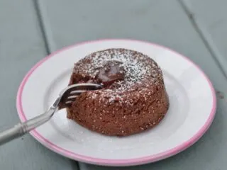 Fork cutting into a molten chocolate cake on a small white plate.