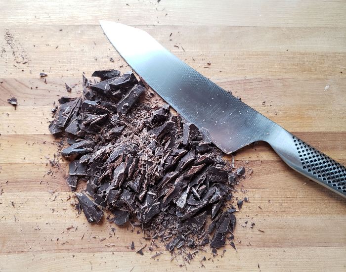 Chopped chocolate on a wooden cutting board with a knife next to it.